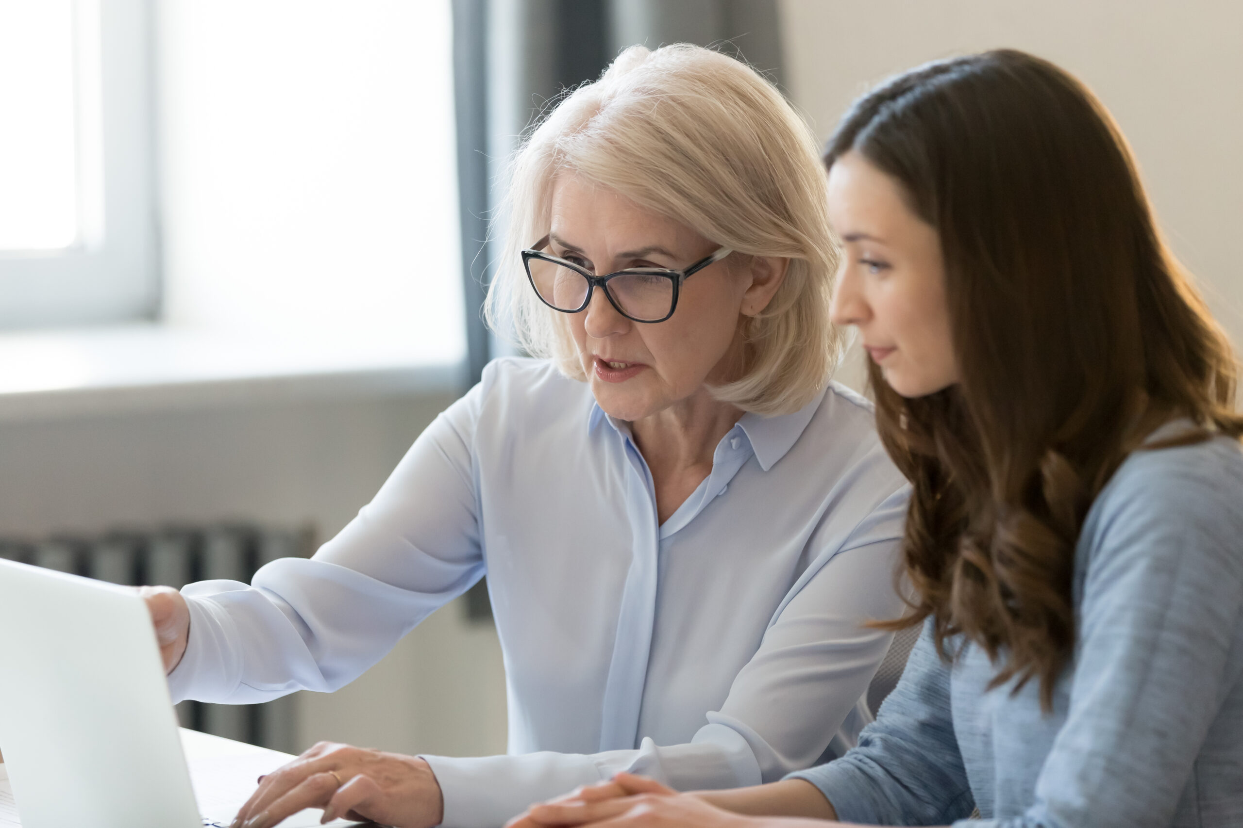 Mature executive manager explaining online project to young employee learning new skills in office